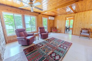 A wooden interior with two recliners, a patterned rug, and large windows.