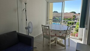 Ein Balkon mit Tisch und Stühlen, einem Standventilator und Blick auf eine Wohngegend.