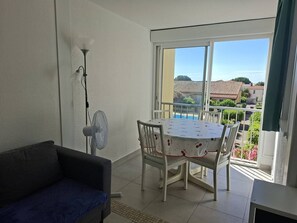 Ein Balkon mit Tisch und Stühlen, einem Standventilator und Blick auf eine Wohngegend.