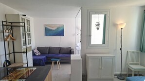 Ein kompaktes Zimmer mit Küchenzeile, einer Couch, einem Esstisch und einem Fenster mit Vorhängen.