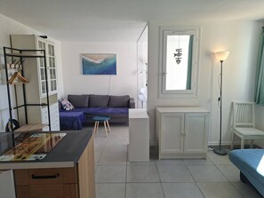 Ein kompaktes Zimmer mit Küchenzeile, einer Couch, einem Esstisch und einem Fenster mit Vorhängen.