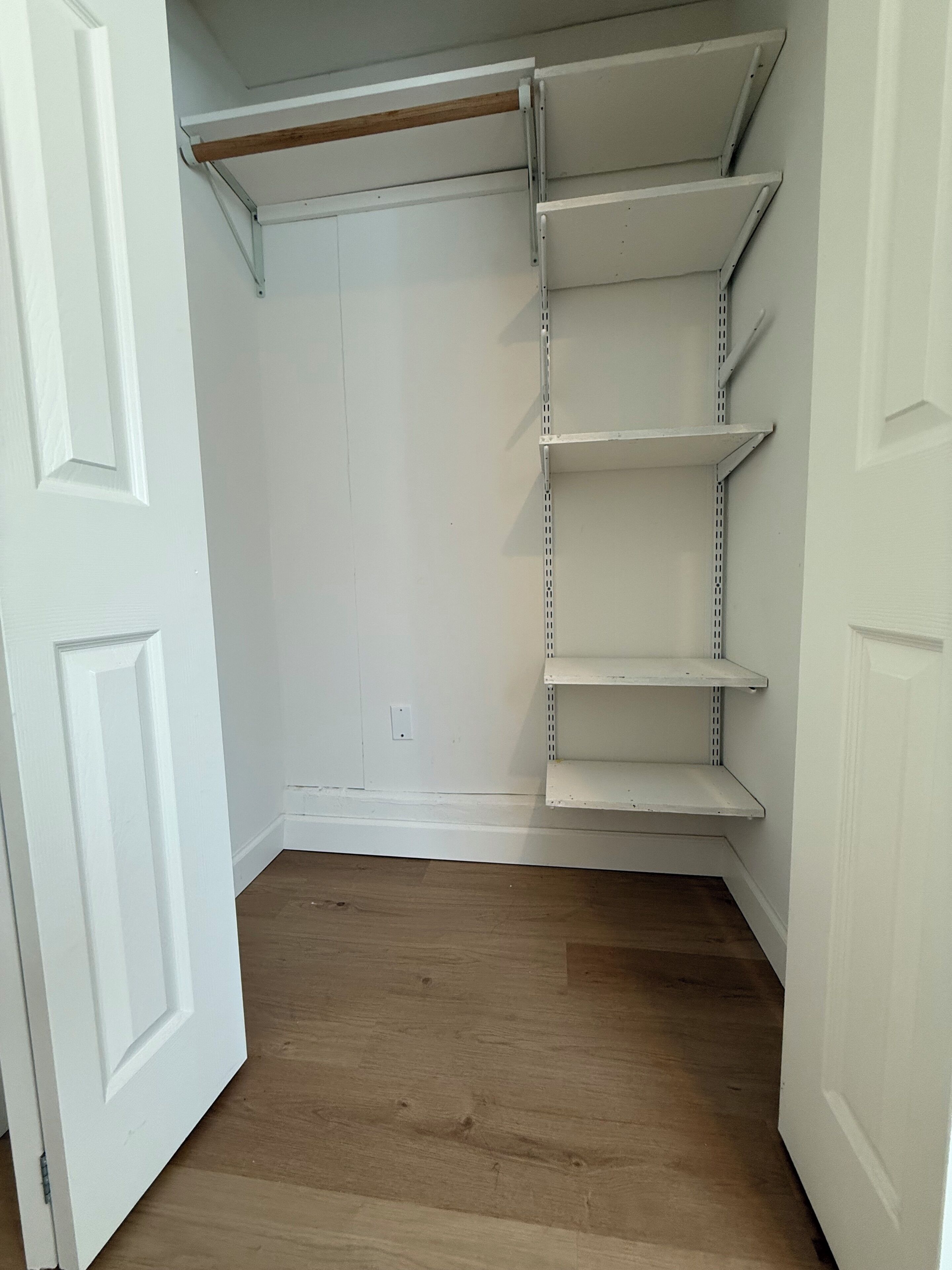A closet with white shelving units and a wooden floor.