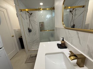 Un bagno con doccia, un lavabo con rubinetto dorato e una parete in marmo.