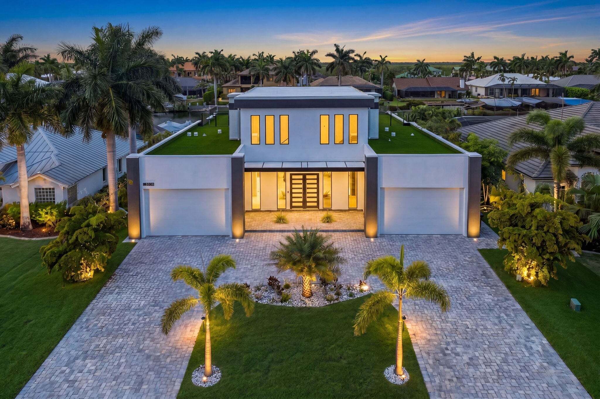 A modern two-story house with a well-maintained lawn, palm trees, and a paved driveway.