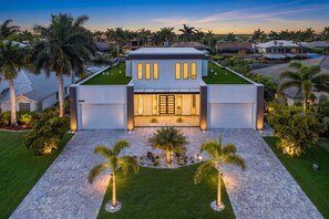 A modern two-story house with a well-maintained lawn, palm trees, and a paved driveway. - Luxury Gulf Access Villa with Pool, Spa & Waterfront Fun Escape - Villa Metropolis - Roelens (Cape Coral)