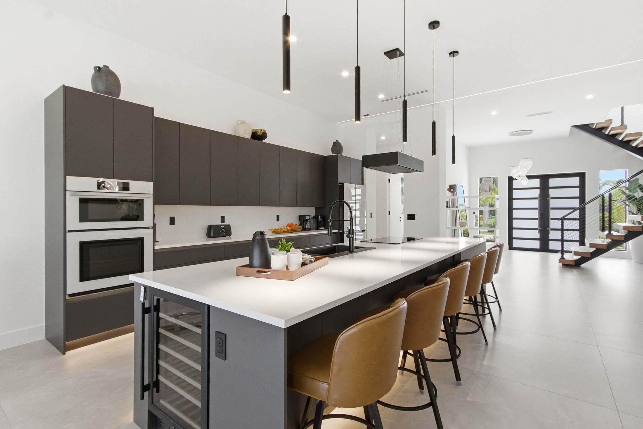 A modern kitchen with a central island, built-in ovens, and a staircase leading to an upper level.