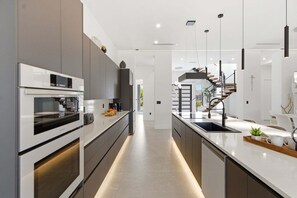 A modern kitchen with built-in appliances, a central island with a sink, and a staircase leading to an upper level. - Luxury Gulf Access Villa with Pool, Spa & Waterfront Fun Escape - Villa Metropolis - Roelens (Cape Coral)