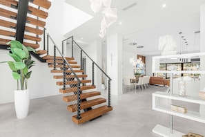 A modern interior with a wooden staircase, a dining area, and a white potted plant. - Luxury Gulf Access Villa with Pool, Spa & Waterfront Fun Escape - Villa Metropolis - Roelens (Cape Coral)