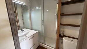 Ein modernes Badezimmer mit Duschkabine aus Glas, einem weißen Waschbecken und einer Holzeinrichtung.