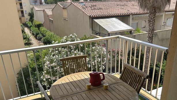 Ein Balkon mit einem runden Holztisch, zwei Stühlen, einem roten Wasserkocher und einer Tasse.