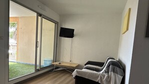 Ein Zimmer mit Glastür zum Balkon, einem flachbildfernseher an der Wand und einem Sofa mit Decke.