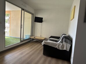 A room with a sliding glass door leading to a balcony, a flat-screen TV mounted on the wall, and a sofa with a blanket. - Lovely 2-bedroom apartment near Richelieu beach, Cap d'Agde (LE CAP D AGDE)
