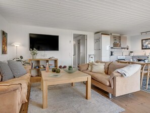 Ein modernes Wohnzimmer mit Sofa, Couchtisch und Fernseher. Es gibt eine Küchenzeile mit Schränken und Geräten.