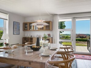 Ein Essbereich mit einem langen Tisch, Stühlen, einer Chandelier und Blick durch Glastüren.
