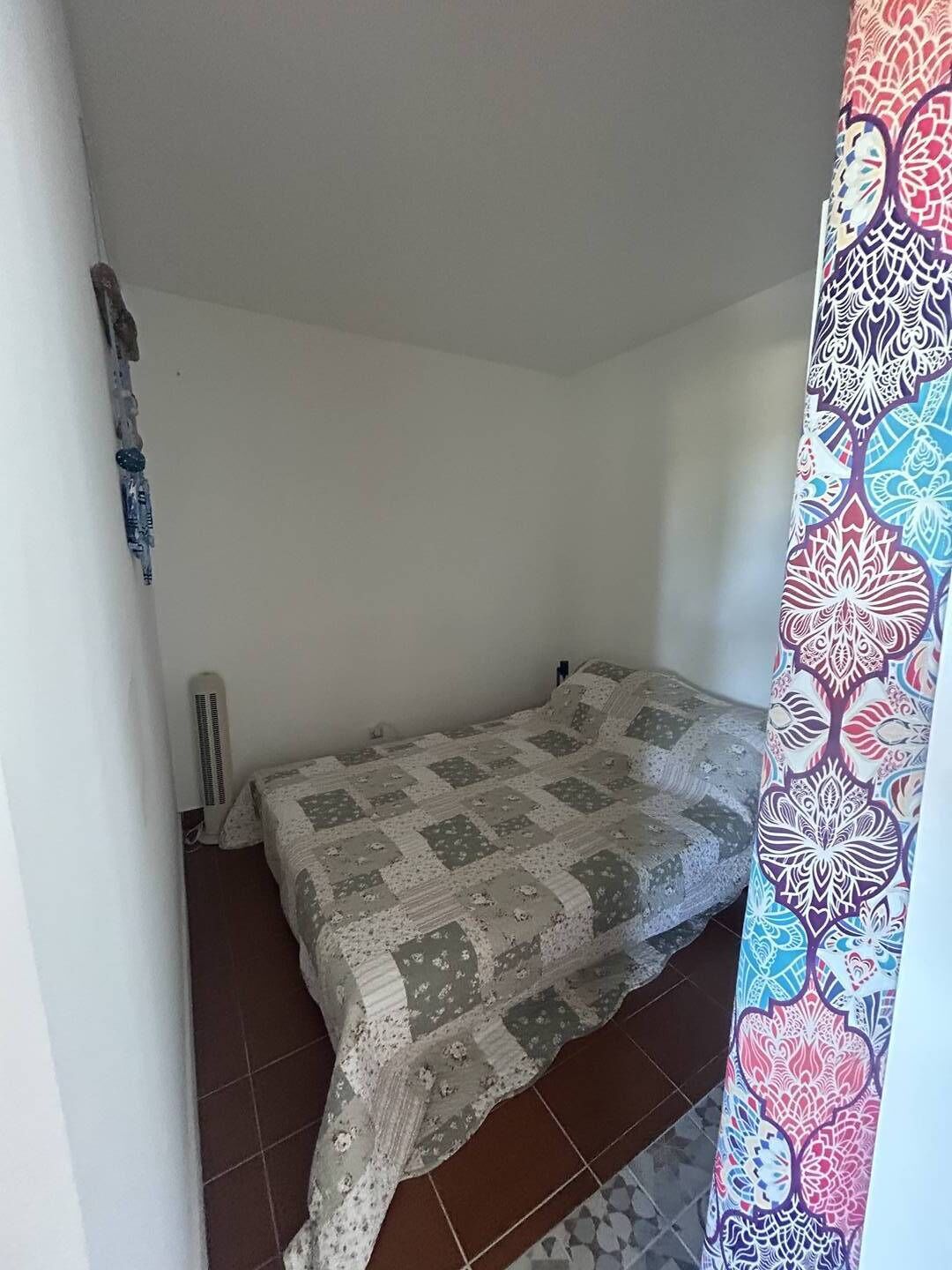 A small, single-bed room with a patterned bedspread, a radiator, and a curtain with a floral design.