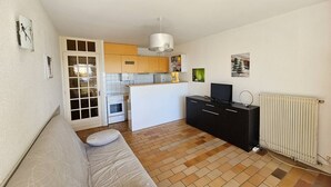 Un espacio habitable compacto con kitchenette, un sofá, un televisor y un radiador.