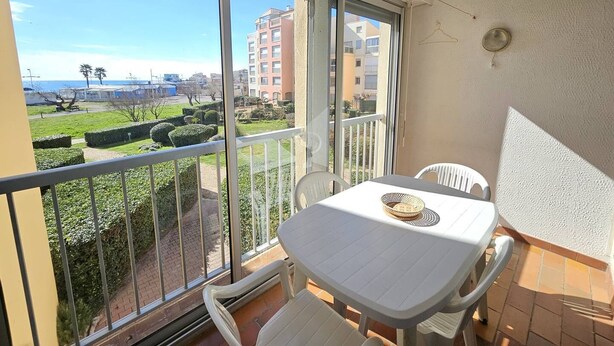 Un balcón con mesa y sillas, vista a un parque y edificios a lo lejos.