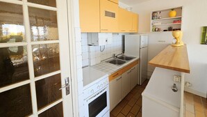 Cocina compacta con armarios blancos y amarillos, horno empotrado, refrigerador y encimera de madera.