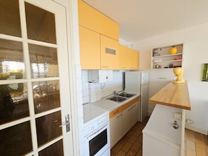 Eine kleine Küche mit weißen und gelben Schränken, einem eingebauten Backofen, einem Kühlschrank und einer Holzarbeitsplatte.