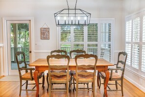 Un comedor con una mesa y sillas de madera, una lámpara colgante y un ventanal con contraventanas.