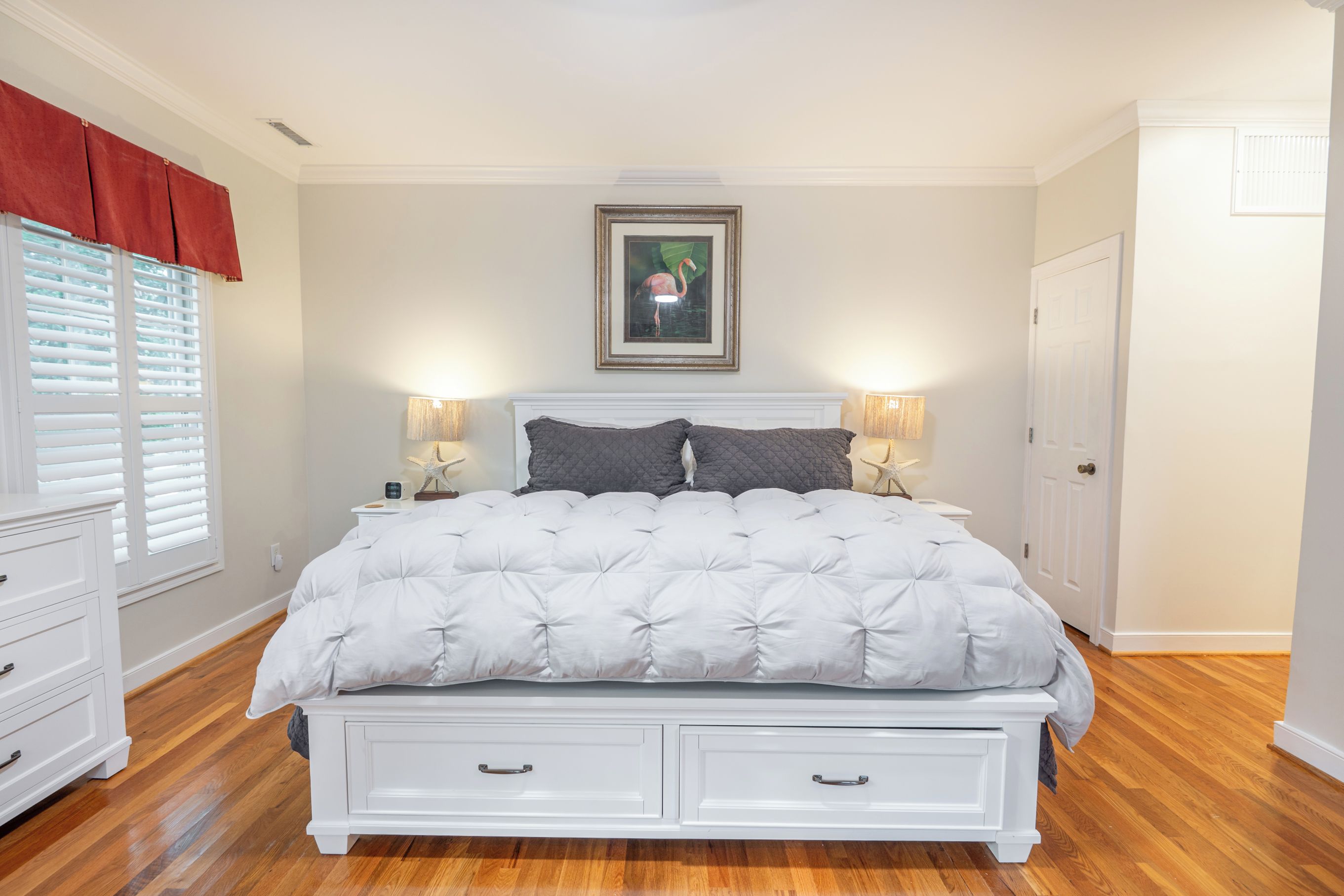 Une chambre à coucher avec un grand lit, deux tables de chevet avec des lampes, une fenêtre avec des stores et une porte.