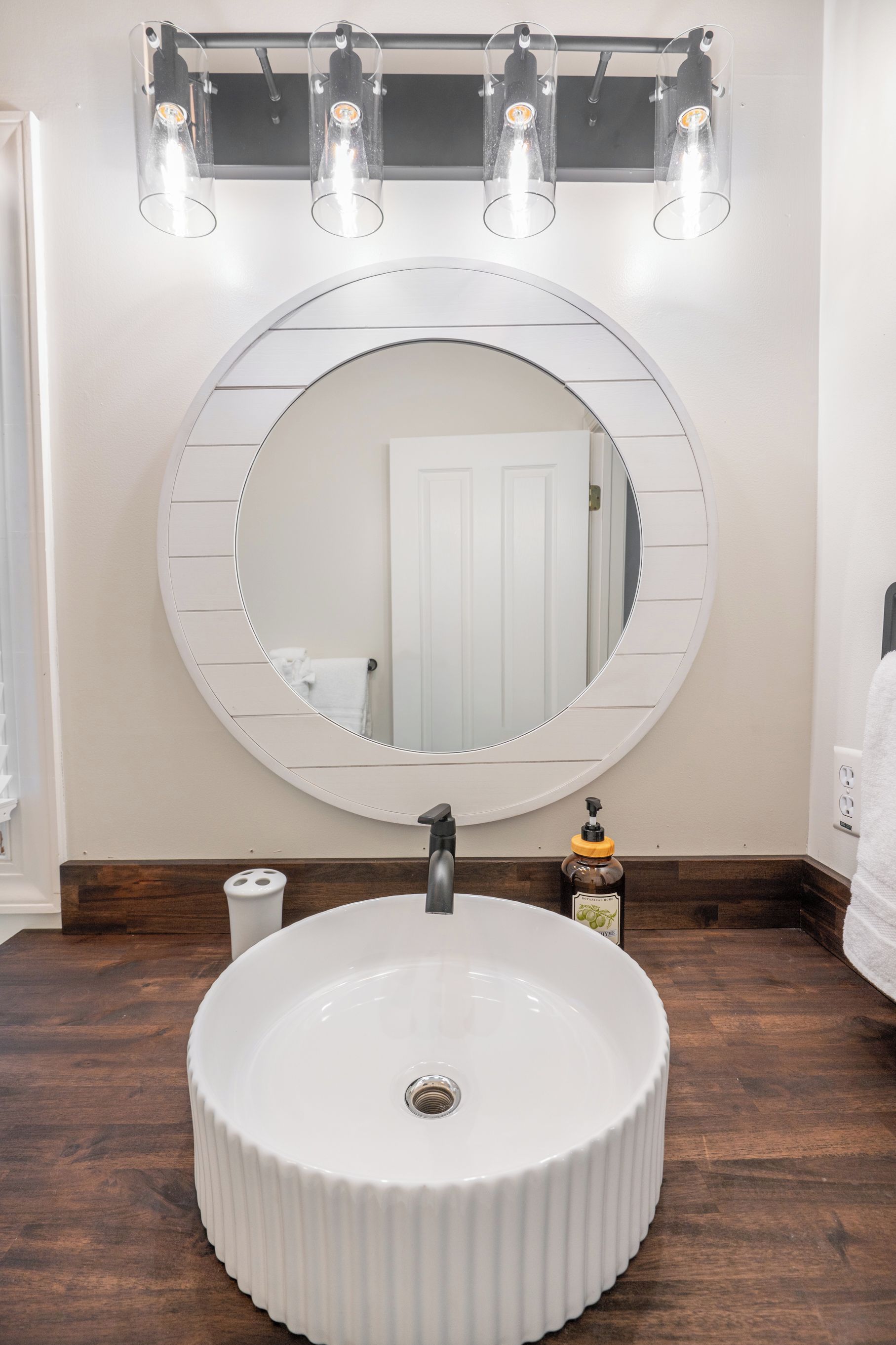 A bathroom with a round mirror, a white sink, and three pendant lights.