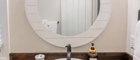 A bathroom with a round mirror, a white sink, and three pendant lights.