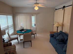 A living room with a pool table, a blue sofa, a lamp, and a ceiling fan.
