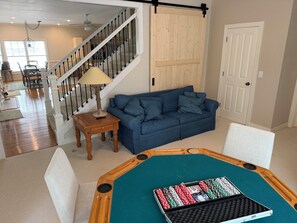 Uma sala de estar com mesa de bilhar, um sofá azul, uma mesa de centro de madeira e uma escada.