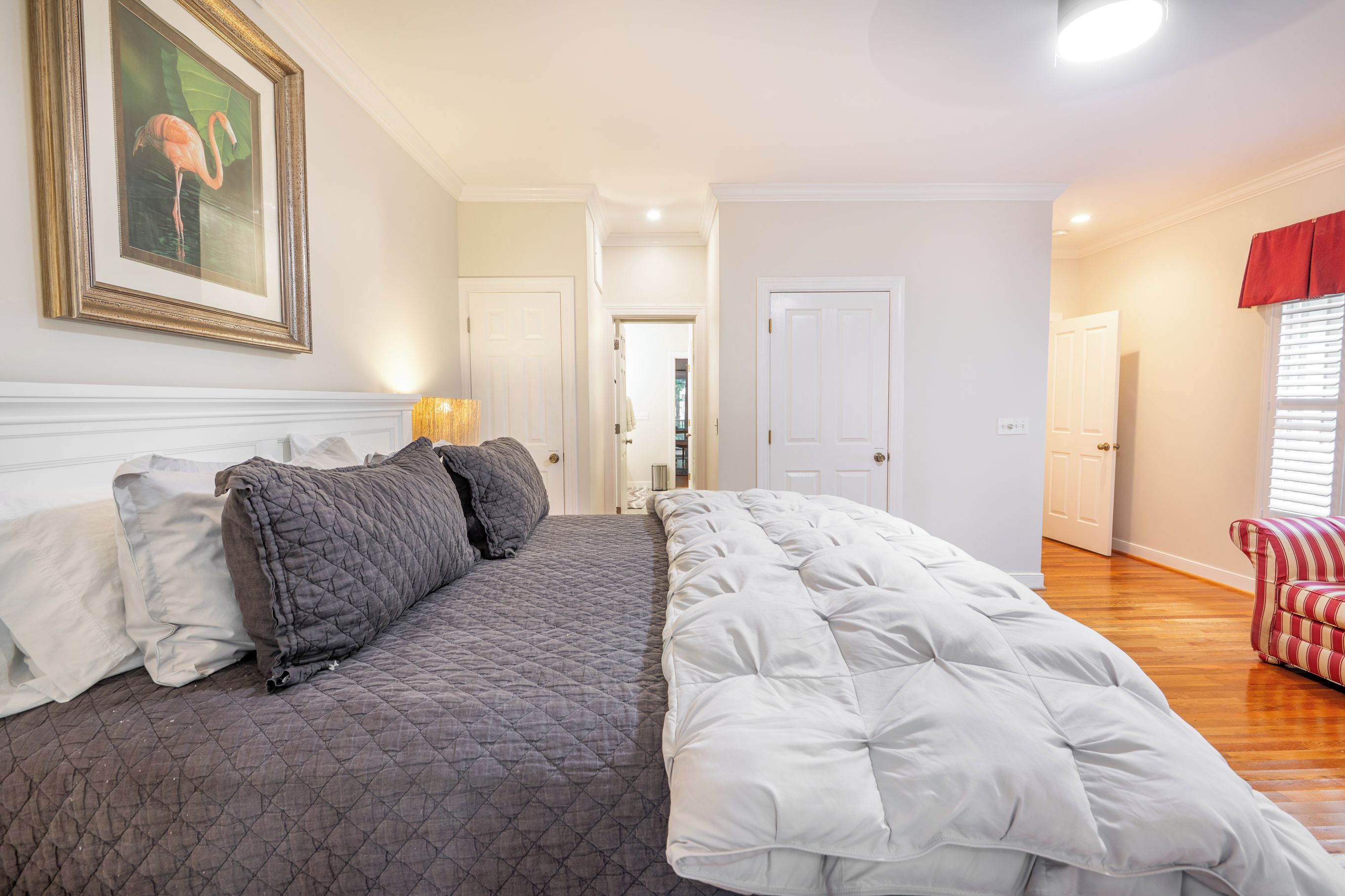 Quarto com uma cama grande, uma porta que dá para outro espaço e uma janela com persianas.