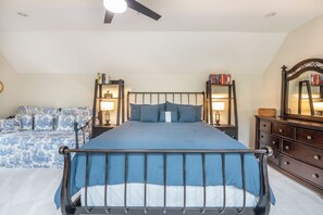 Un dormitorio con cama, mesitas de noche, cómoda, espejo y ventilador de techo.