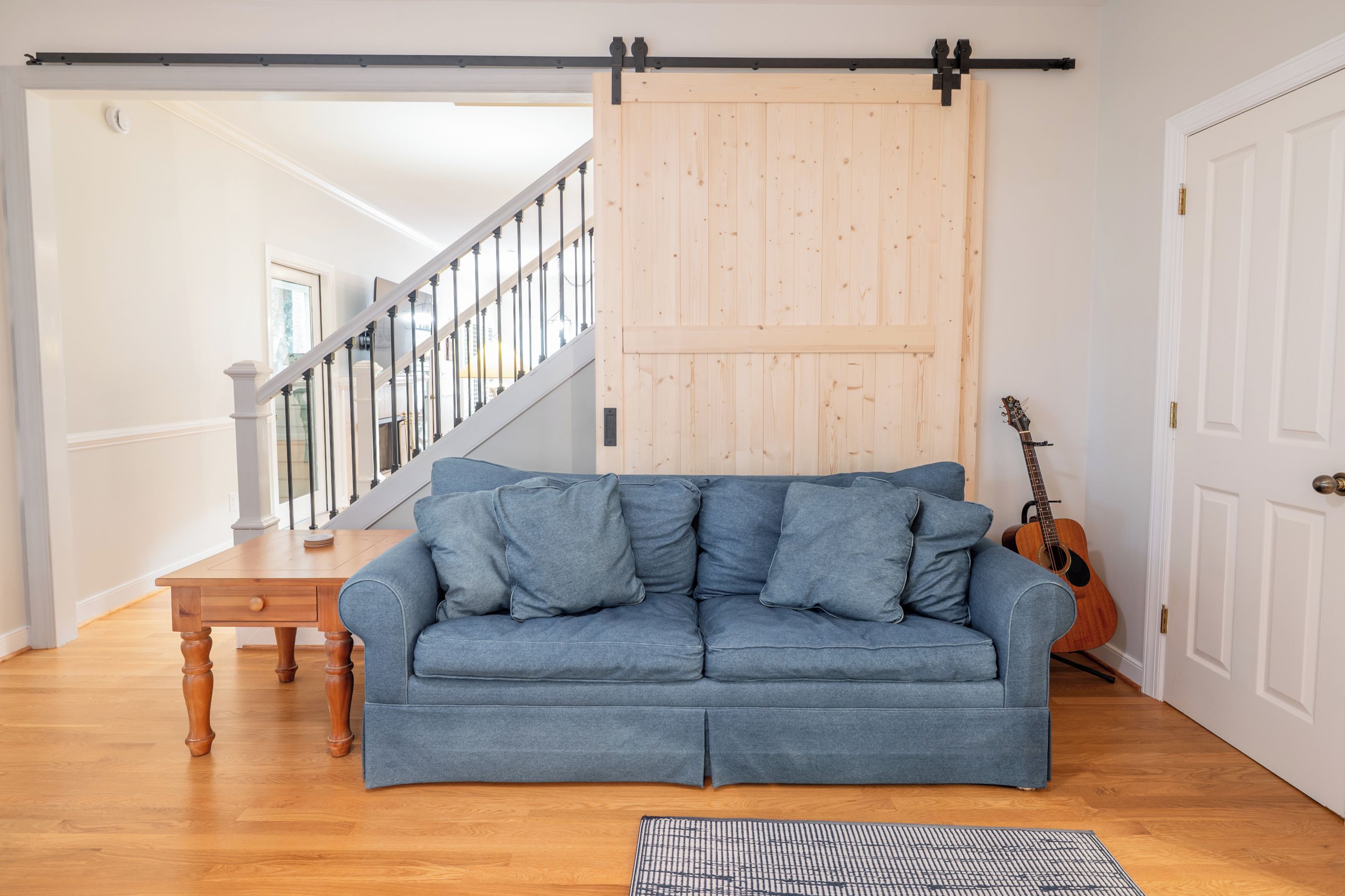 Una habitación con un sofá azul, una mesa de madera, una guitarra y una puerta corredera.