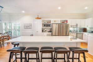 Una cocina moderna con una isla grande, taburetes de bar, muebles blancos y electrodomésticos de acero inoxidable.