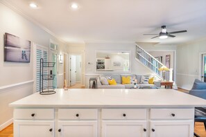 A spacious living area with a central island, a staircase, and a kitchen in the background.