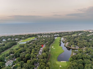 Un parcours de golf avec un obstacle d’eau, entouré de propriétés résidentielles et bordé d’une plage.