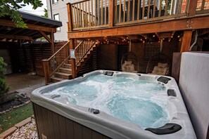 Ein Whirlpool in einem Garten mit einer Holzterrasse und einer Treppe zu einem überdachten Bereich.
