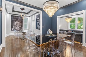Un coin repas avec une table à plateau en verre, des chaises transparentes et un lustre.
