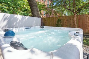 Un bain à remous dans un jardin, avec une clôture en bois et des arbres.