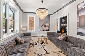 Un salon moderne avec un lustre, deux canapés gris, une table basse et une grande fenêtre.