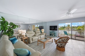 Ein modernes Wohnzimmer mit einer Couch, Sesseln, einem Couchtisch, einem Fernseher und einem Balkon mit Blick.