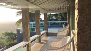 Un espace extérieur aménagé avec des sièges, protégé du soleil, comprenant des chaises en osier, une piscine et une vue sur l’océan.