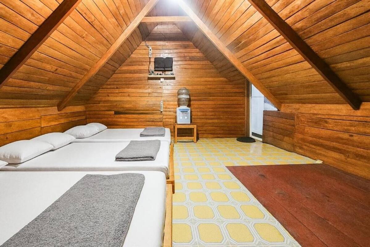 A cozy attic bedroom with wooden walls, two beds, a heater, and a window.