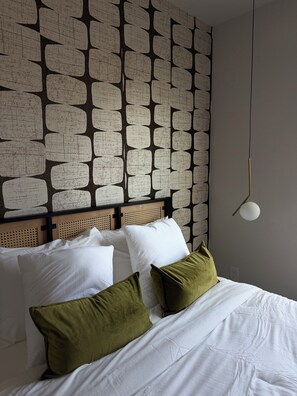 A bed with white bedding and green pillows, a headboard with a woven pattern, and a wall with a geometric design.