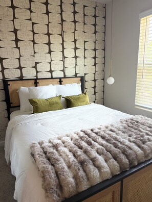 Une chambre avec un papier peint à motifs, un lit recouvert d’une literie blanche et une couverture douce et moelleuse.