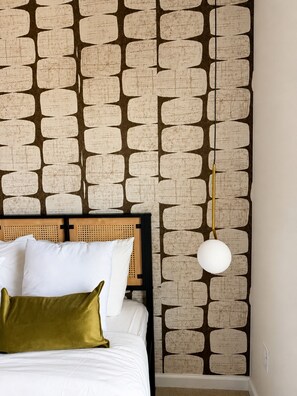 A bed with white bedding and a green pillow, a headboard with a woven pattern, and a wall with a geometric pattern.