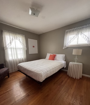 Ein Schlafzimmer mit einem Bett, einem Nachttisch, einem Sessel und einem Fenster mit Vorhängen.