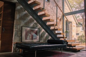 A modern interior with a stone wall, a staircase, a bench, and a framed picture. - 4 BR Architectural Home | 3 min from ACL (Austin)