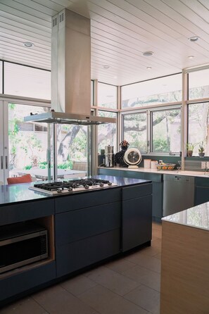 Una cucina moderna con isola centrale, elettrodomestici integrati e ampie finestre che danno su una vista verde.