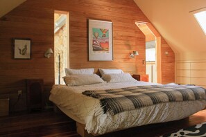 Una camera da letto con soffitto in legno, un letto con coperta a quadri, un quadro appeso al muro e una finestra con vista.