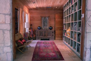 Una stanza accogliente con soffitto in legno, una grande libreria, un tappeto decorato, un angolo con divanetto e un violino.